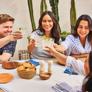 Gruppe junger Menschen stößt mit Teremana Margaritas an, Outdoor-Tisch mit Kaktus-Hintergrund