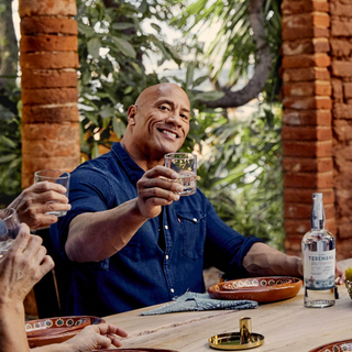 Teremana-Gründer Dwayne Johnson lächelt und hebt sein Glas Tequila bei einem geselligen Abend