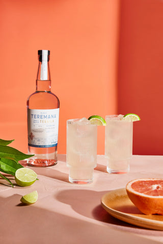 Mana Paloma mit Teremana Blanco Tequila: zwei Highball-Drinks mit Limette, Grapefruit, orangefarbener Hintergrund